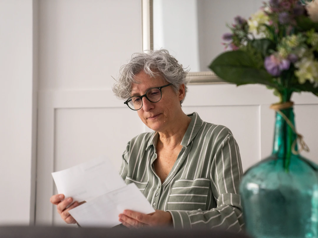Foto en la que sale una mujer mirando papeles. En la mesa hay flores.
