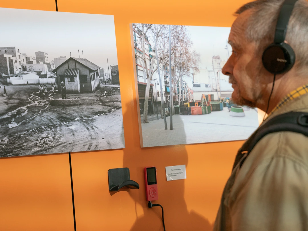 Una persona mira dos fotos colgadas en la pared y escucha un audio con unos auriculares que cuelgan directamente de la pared.