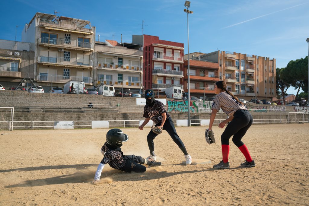 Foto d'un instant d'un partit de baseball. Un noi arrica derrapant a la base mentre uns altres dos següeixen la jugada.