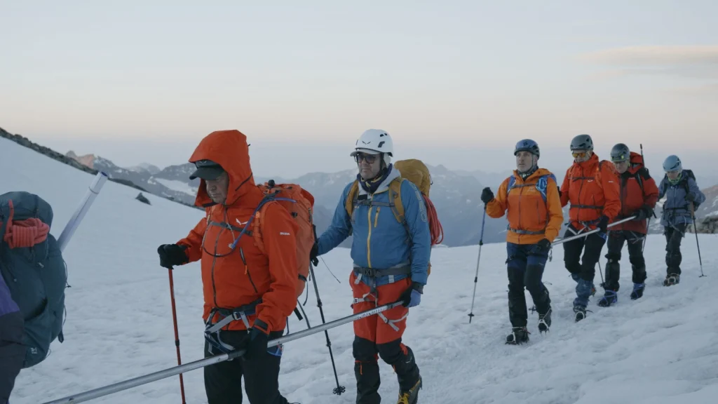 Foto de dos grups de persones, agafant les barres direccionals, vestides d'alpinisme, en una muntanya nevada.
